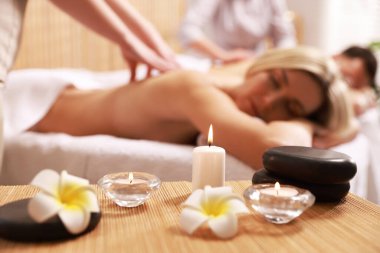 Spa salonunda masaj yaptıran çift mum, çiçek ve taş yakmaya odaklanıyor.