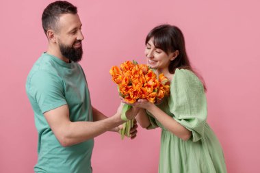 Adam pembe arka planda sevgili karısına bir buket güzel lale sunuyor.