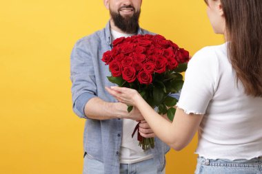 Adam turuncu arka planda sevgilisine kırmızı gül buketi sunuyor.