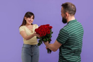 Adam mor arka planda sevgili karısına kırmızı güller sunuyor.