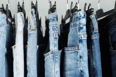Many stylish jeans hanging from rack on white background, closeup
