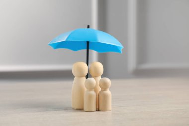 Şemsiyenin altındaki insan figürleri açık tahta masada. Sigorta konsepti