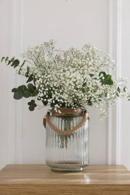 Beautiful gypsophila flowers and eucalyptus branches in vase on table at home