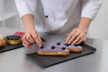 Pasta şefi, içerideki masada yabanmersinli pasta dekorasyonu yapıyor, yakın plan.