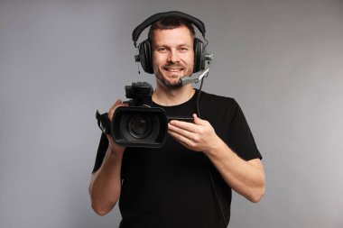 Profesyonel kameralı ve kulaklıklı bir adam gri arka planda.