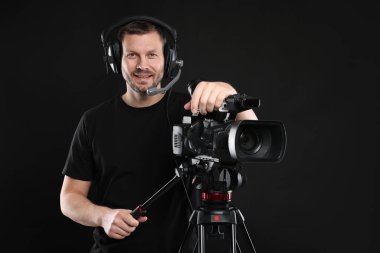 Profesyonel kameralı ve kulaklıklı bir adam siyah arka planda.