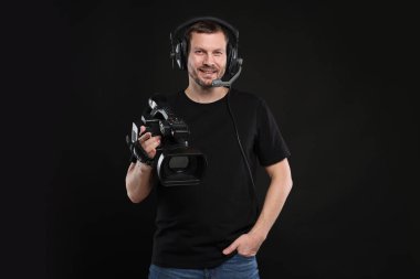 Profesyonel kameralı ve kulaklıklı bir adam siyah arka planda.