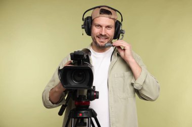 Profesyonel kamera ve soluk zeytinli arka planda kulaklığı olan bir adam.