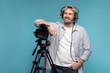 Profesyonel video kamerası ve açık mavi arka planda kulaklığı olan bir adam.