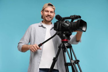 Açık mavi arka planda profesyonel video kamerası olan adam.