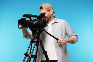 Açık mavi arka planda profesyonel video kamerası olan adam.