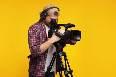 Profesyonel kamera ve turuncu arka planda kulaklığı olan bir adam.