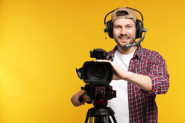 Profesyonel video kamerası ve turuncu arka planda kulaklığı olan adam, metin için boşluk