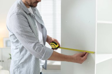 Beyaz rafları bantla ölçen adam içeride, yakın plan.
