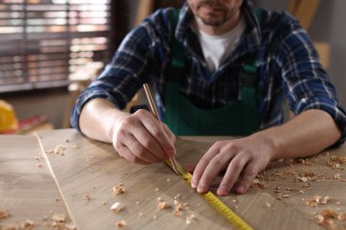 İçerideki ahşap masada bant ve kalemle tahta ölçen adam, yakın plan.