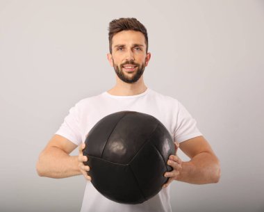 Açık gri arka planda tıp topu olan atletik bir adam.