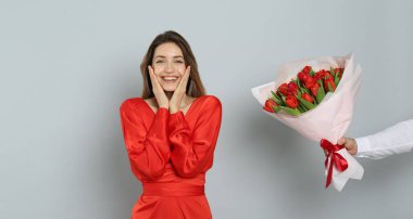 Mutlu kadın açık gri arka plandaki adamdan kırmızı lale buketi alıyor. 8 Mart kutlamaları