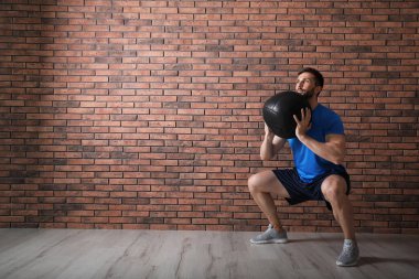 Kaslı adam kırmızı tuğla duvarın yanında ilaç topuyla çömeliyor, mesaj için yer var.