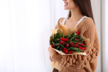 Kapalı alanda kırmızı lale çiçekli mutlu kadın, yakın plan. 8 Mart kutlamaları