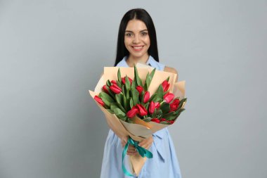 Açık gri arka planda kırmızı lale çiçekli mutlu kadın. 8 Mart kutlamaları