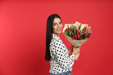 Kırmızı arka planda lale çiçekleri olan mutlu bir kadın. 8 Mart kutlamaları