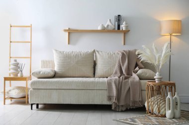 Yastıklı, battaniyeli, lambalı ve beyaz duvarlı rahat bir kanepe. İç tasarım