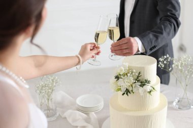 Evde düğün pastası olan evli bir çift şampanya bardaklarını tokuşturuyor.