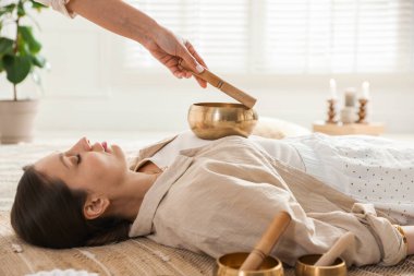 Şarkı söyleyen kadın kase terapisi görüyor. Kapalı yerde yatıyor.