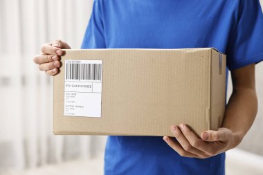Kapalı alanda nakliye etiketli bir paket taşıyan adam.