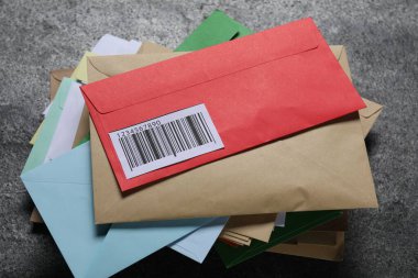 Koyu gri masanın üzerinde, görüş alanının üstünde farklı kağıt zarflar yığını var. Postane