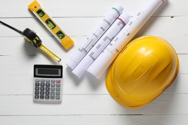 Farklı teknik çizimler, sabit şapka, hesap makinesi, bina seviyesi ve mezura beyaz ahşap masa üzerinde düz yatıyordu.