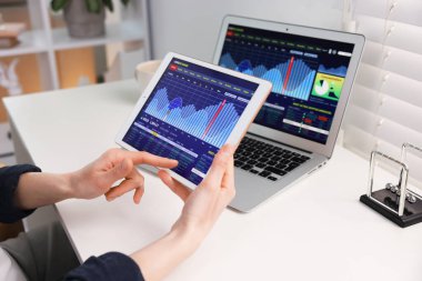 Borsa. Kadın, kapalı bir masada, tablet üzerinde finansal piyasayı analiz ediyor.