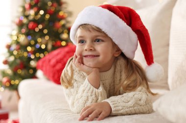 Noel Baba şapkalı küçük kız evdeki kanepede yatıyor.