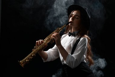 Karanlık arka planda dumanla soprano saksafon çalan müzisyen.