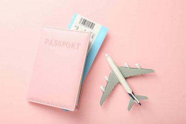 Pasaport ve uçak modeli pembe arka planda, düz yatıyordu.