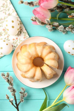 Lezzetli bohça keki, Paskalya yumurtaları, söğüt dalları ve açık mavi ahşap masa üzerindeki laleler.