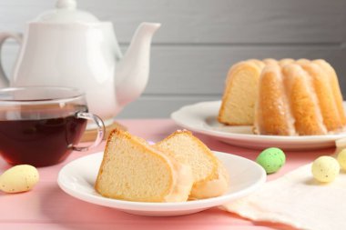 Lezzetli kek parçaları, pembe ahşap masada paskalya yumurtası ve çay.