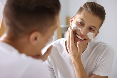 Banyoda aynanın yanında yüzünü kozmetik ürünlerle yıkayan adam.