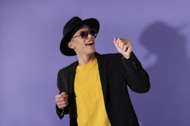 Güneş gözlüklü mutlu adam menekşe arka planda dans ediyor.