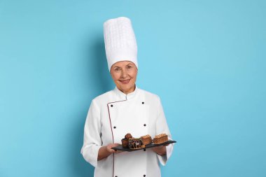 Açık mavi arka planda tatlıları olan profesyonel pasta şefi.
