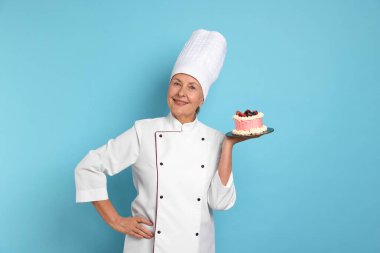 Açık mavi arka planda pastası olan profesyonel pasta şefi.