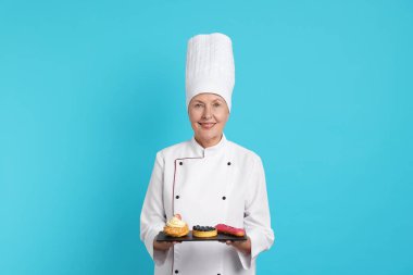 Açık mavi arka planda tatlıları olan profesyonel pasta şefi.