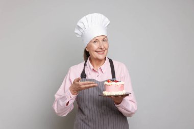 Açık gri arkaplanda pasta gösteren profesyonel bir şekerci.