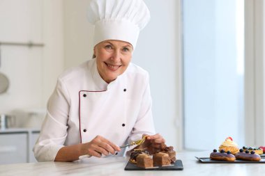 Gülümseyen pasta şefi mutfaktaki masada yenilebilir altın yaprak örtüsüyle lezzetli tatlılar süslüyor.