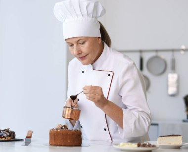 Mutfaktaki masada erimiş çikolatayla pasta süsleyen kıdemli pasta şefi