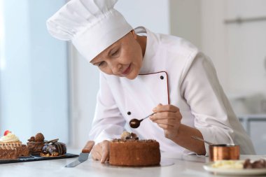 Mutfaktaki masada erimiş çikolatayla pasta süsleyen kıdemli pasta şefi