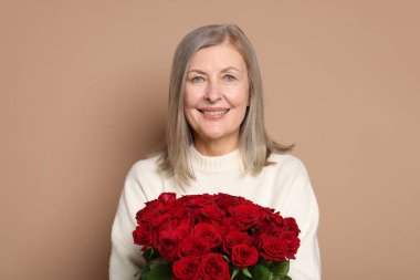 Bej arka planda bir buket gülle gülümseyen kadın.