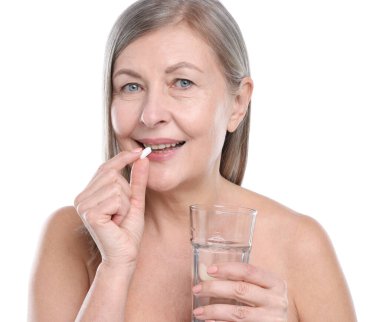 Bir bardak suyla gülümseyen kadın beyaz arka planda kolajen hapı alıyor.