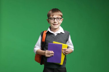 Sırt çantası ve yeşil arka plan kitapları olan tatlı bir okul çocuğu.