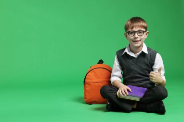 Sırt çantalı ve kitaplı mutlu okul çocuğu yeşil arka planda başparmak gösteriyor, mesaj için yer var.